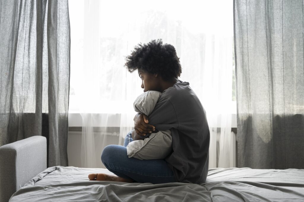 Mulher jovem negra está deprimida e abraça um travesseiro sobre um leito